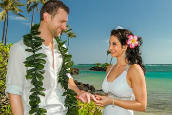 Bride putting ring on maile lei groom